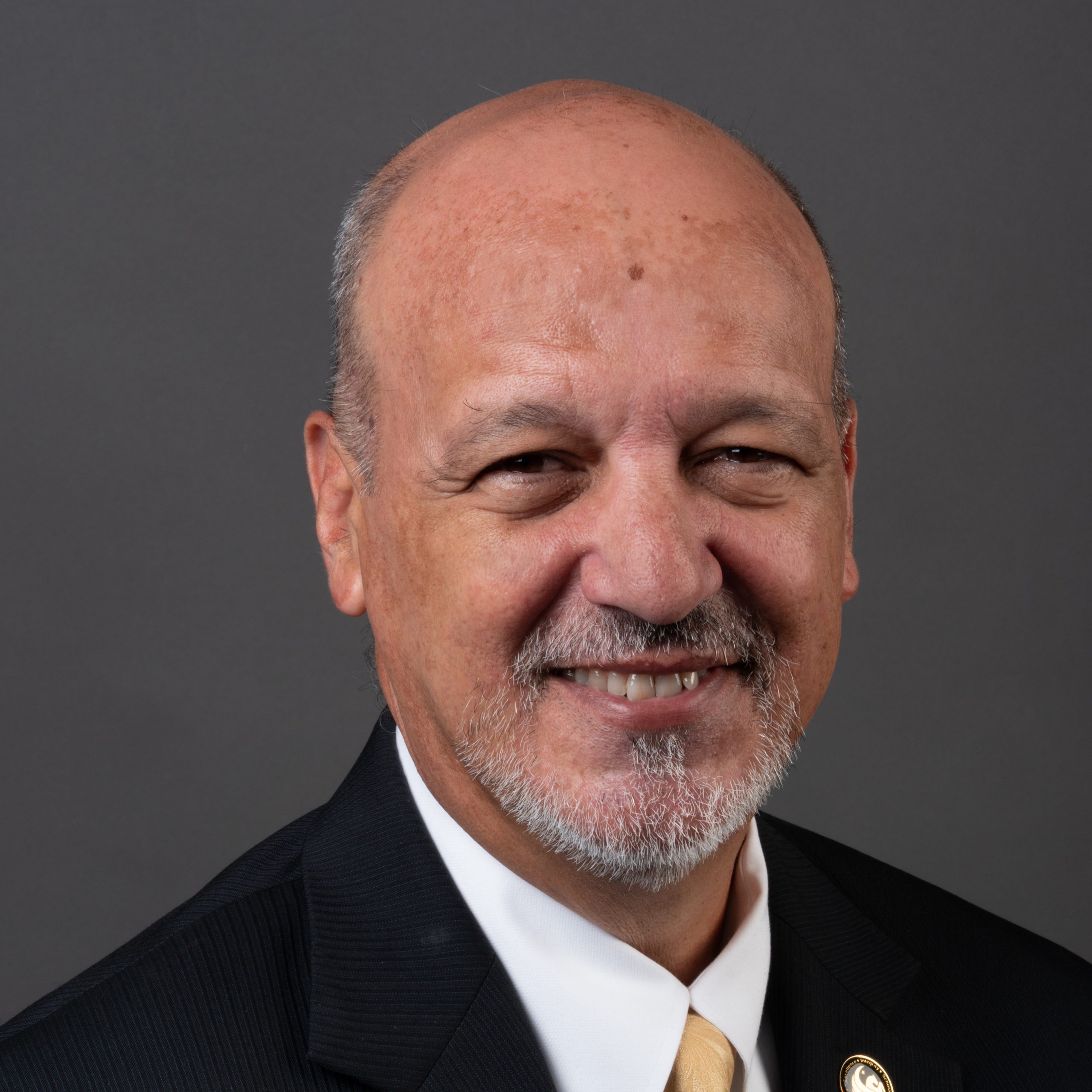 Paul Dosal is a Cuban-American man wearing a black suit and gold tie